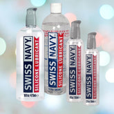 Displayed against a blurred background are four bottles of the Swiss Navy Silicone Lubricant, renowned for its enduring glide. These lubricants, characterized by their distinctive red and blue labels, offer a silky experience every time and come in sizes ranging from 2 oz to 32 oz.